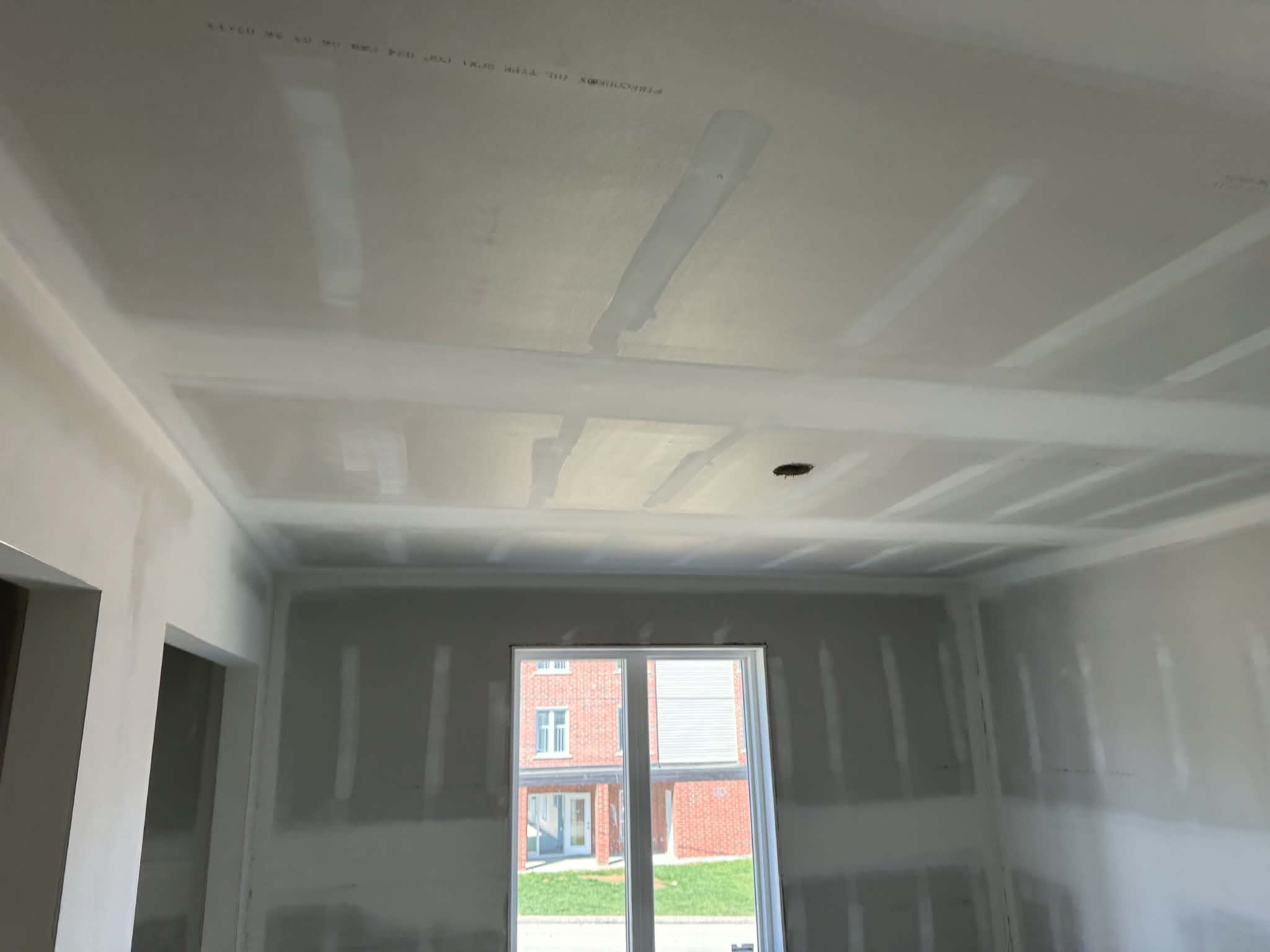 Plafond près d'une fenêtre donnant sur un immeuble de brique, joints de gypse en cours de finition